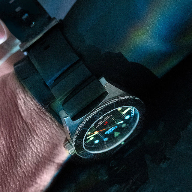 Close-up of the Timex Deepwater Reef 200 dive watch on a diver’s wrist partially submerged, illuminated by shifting blue-green underwater light.