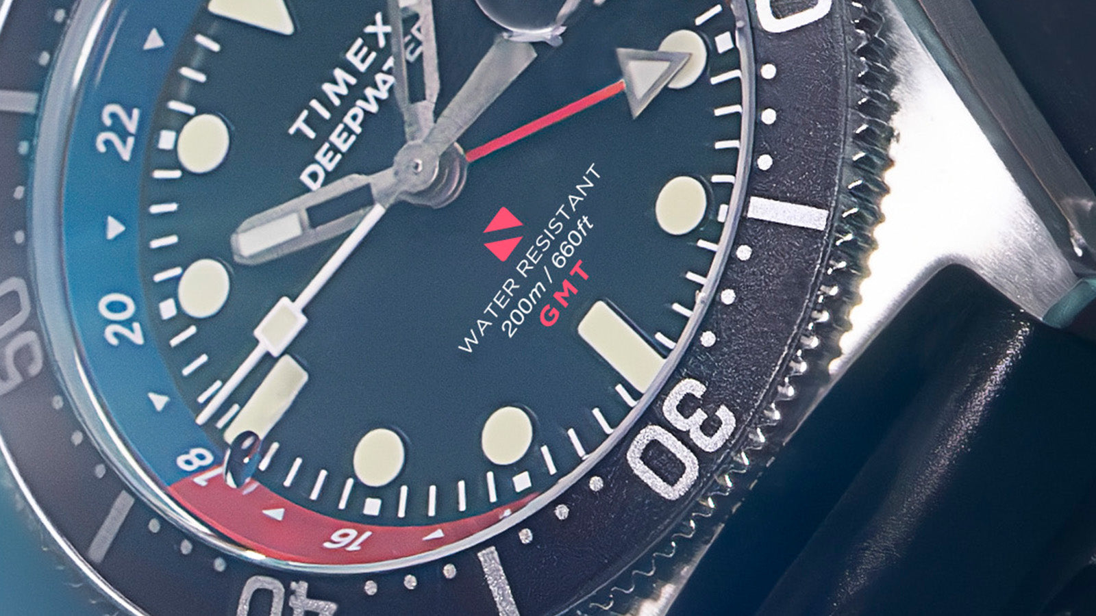 Macro shot of the Timex Deepwater Reef 200 GMT dial highlighting the red GMT hand, blue and red bezel, and “Water Resistant 200m / 660ft” engraving.