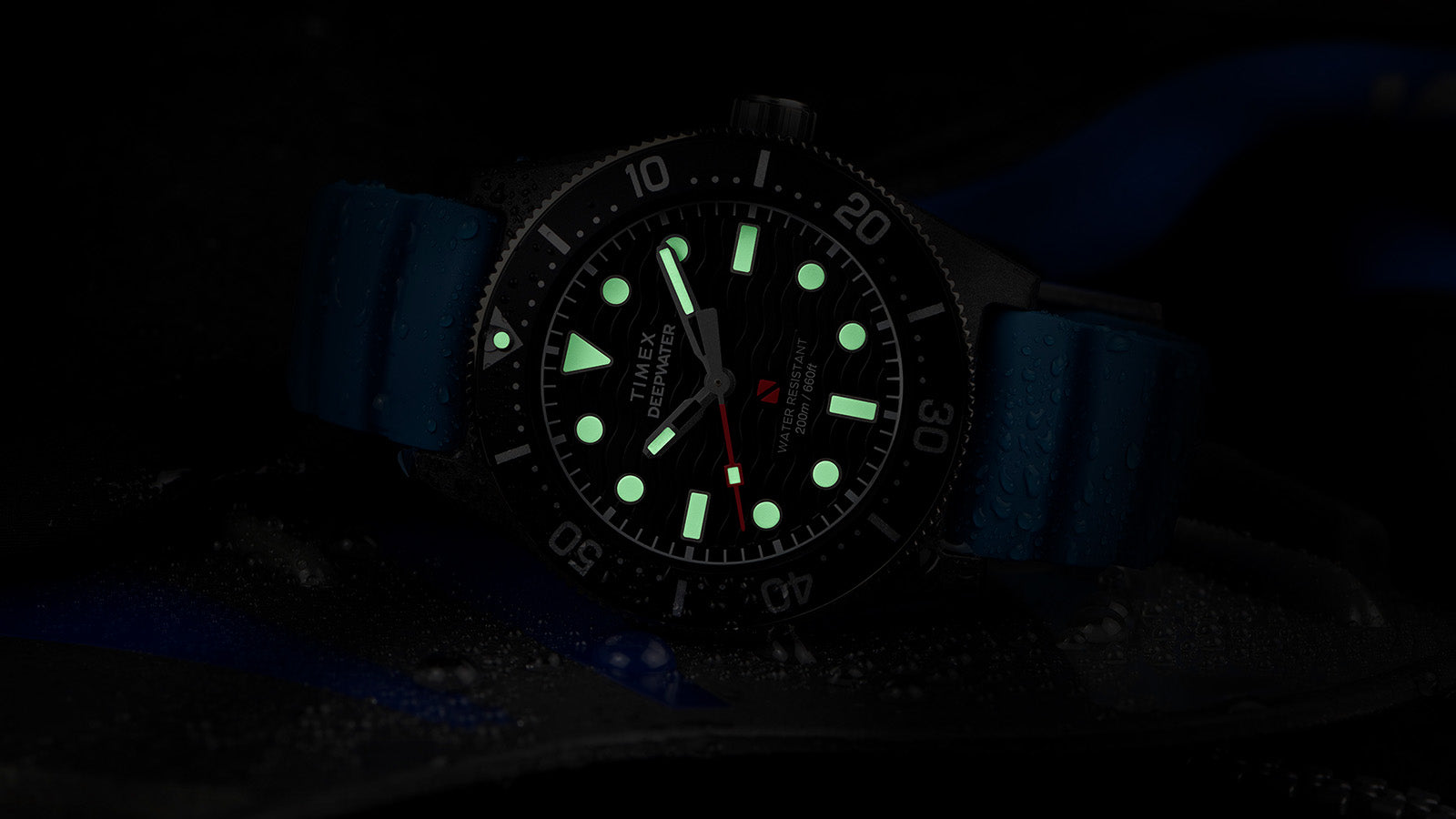 Timex Deepwater Reef 200 XCF glowing in the dark, with luminous green hands and markers visible against the black dial for underwater readability.