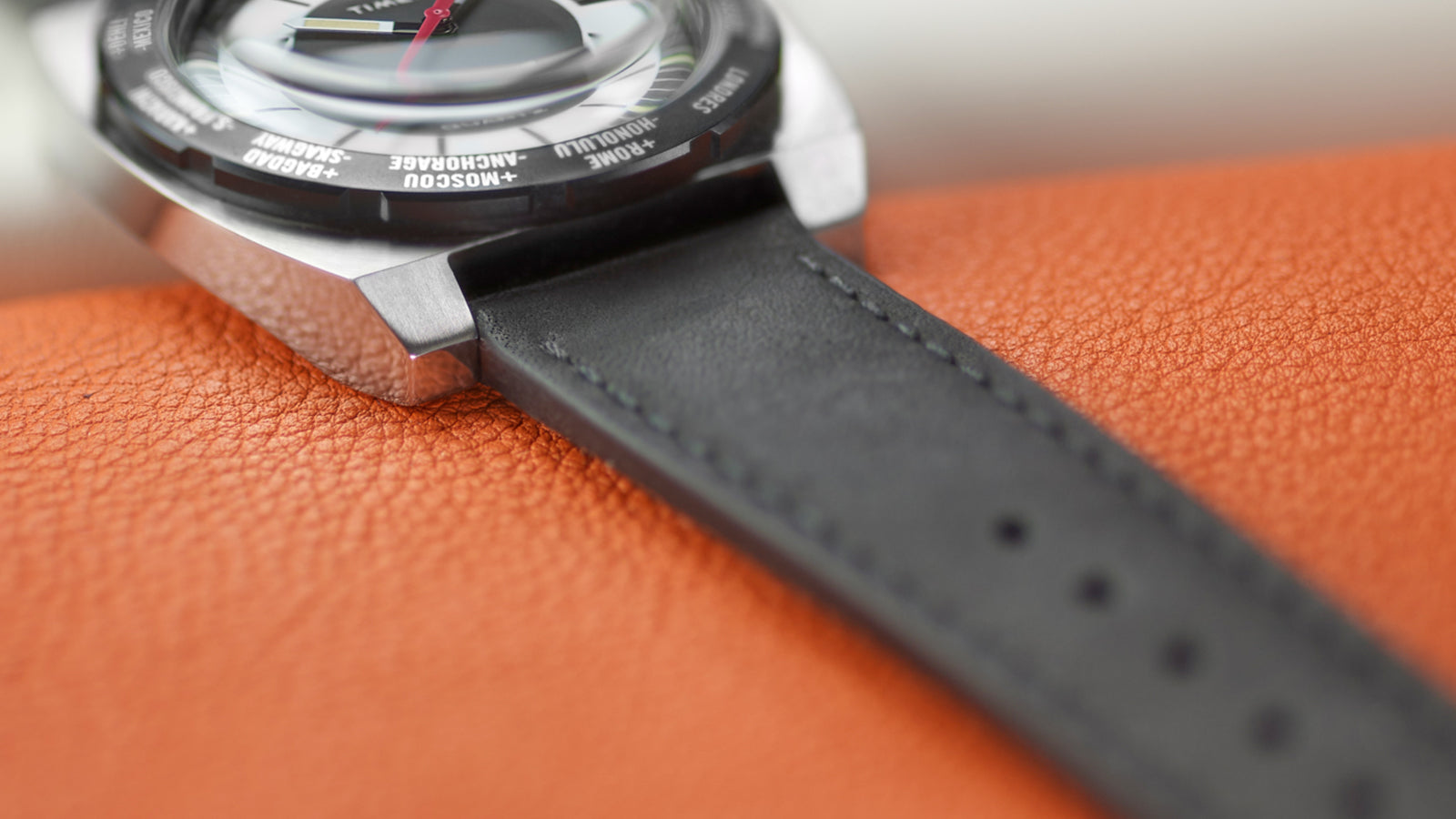 Close-up of the Timex World Time Reissue watch’s lug and strap connection, showing the brushed steel edge, black leather band stitching, and domed crystal curvature.