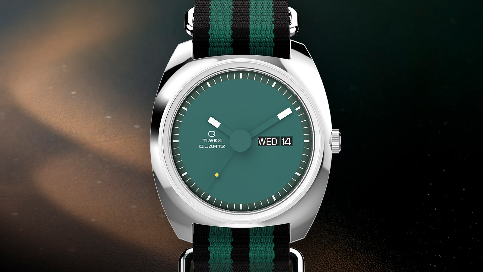 Front view of the Q Timex® 1975 Enigma featuring a teal dial, day-date window, and black-and-green NATO-style strap with a polished stainless-steel case.