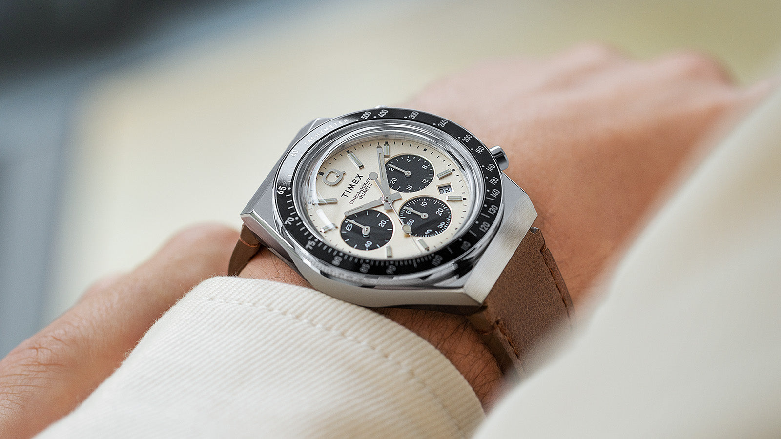 Side view of the Q Timex Chronograph on wrist, emphasizing the polished stainless steel case, cream dial, and black tachymeter bezel.
