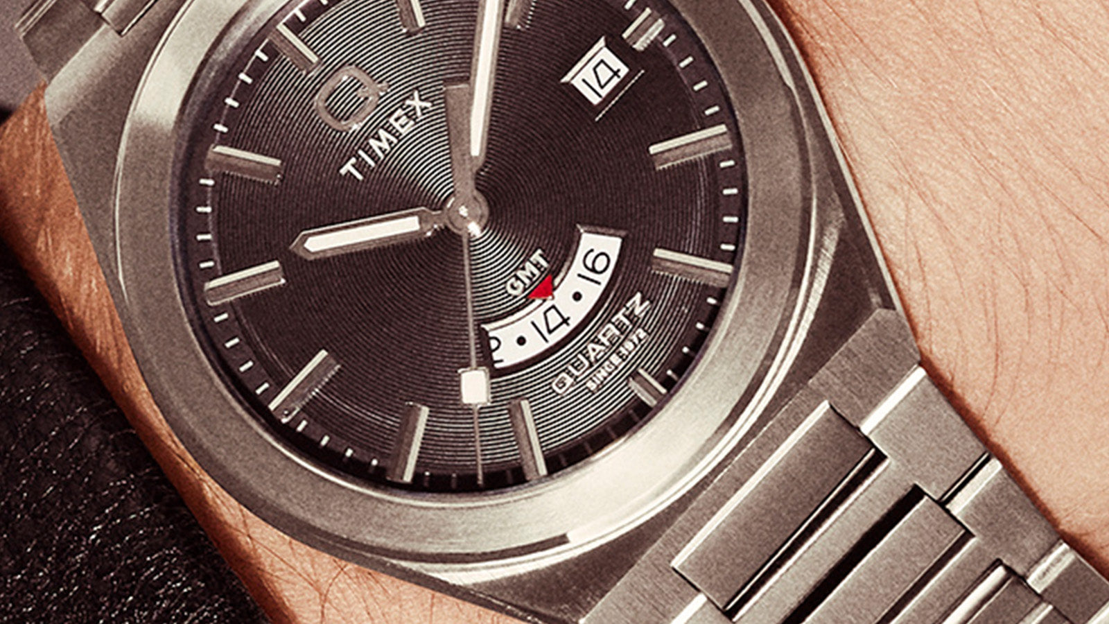 Macro shot of the Q Timex® Continental GMT dial highlighting the concentric texture, GMT subdial with red accent, and precision-applied hour markers.