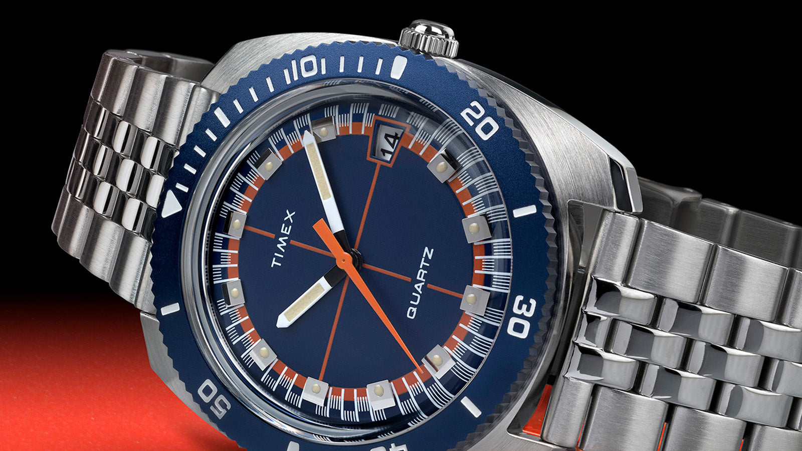 Side angle view of the Q Timex® 1971 Velocity watch highlighting the brushed stainless steel case, blue bezel, and retro racing color scheme.