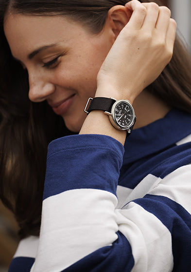 A woman smiling while wearing a Timex Weekender with a black dial and black fabric strap, paired with a navy and white striped top.