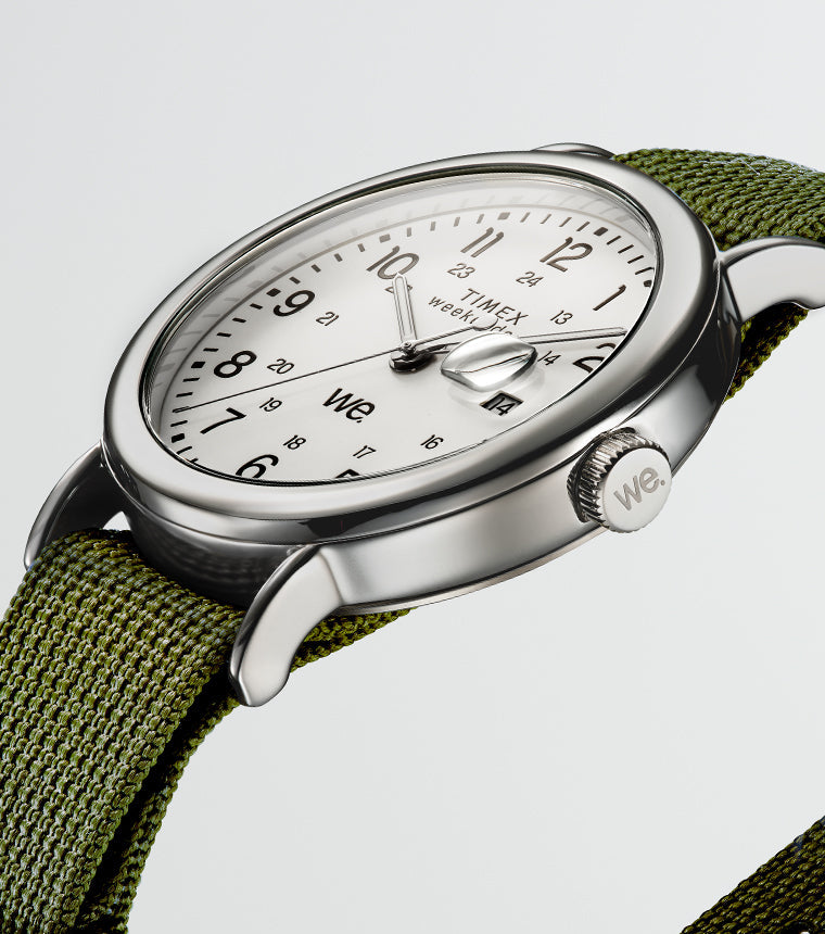 Angled view of a Timex Weekender watch with a green fabric strap, silver-tone case, and white dial with black numerals.