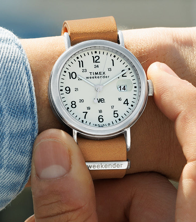 Person adjusting the crown of a Timex Weekender watch with white dial and tan leather strap, close-up wrist shot.