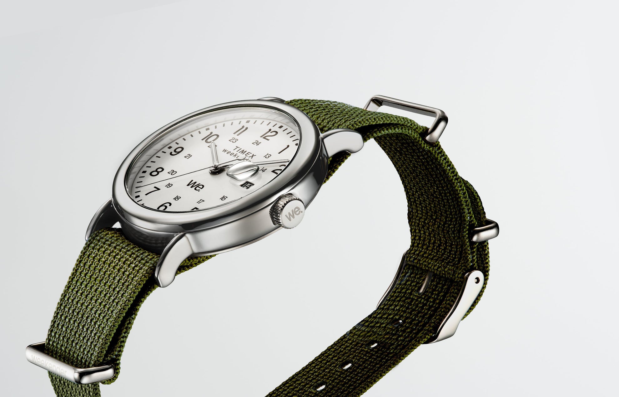 Angled view of a Timex Weekender watch with a green fabric strap, silver-tone case, and white dial with black numerals.