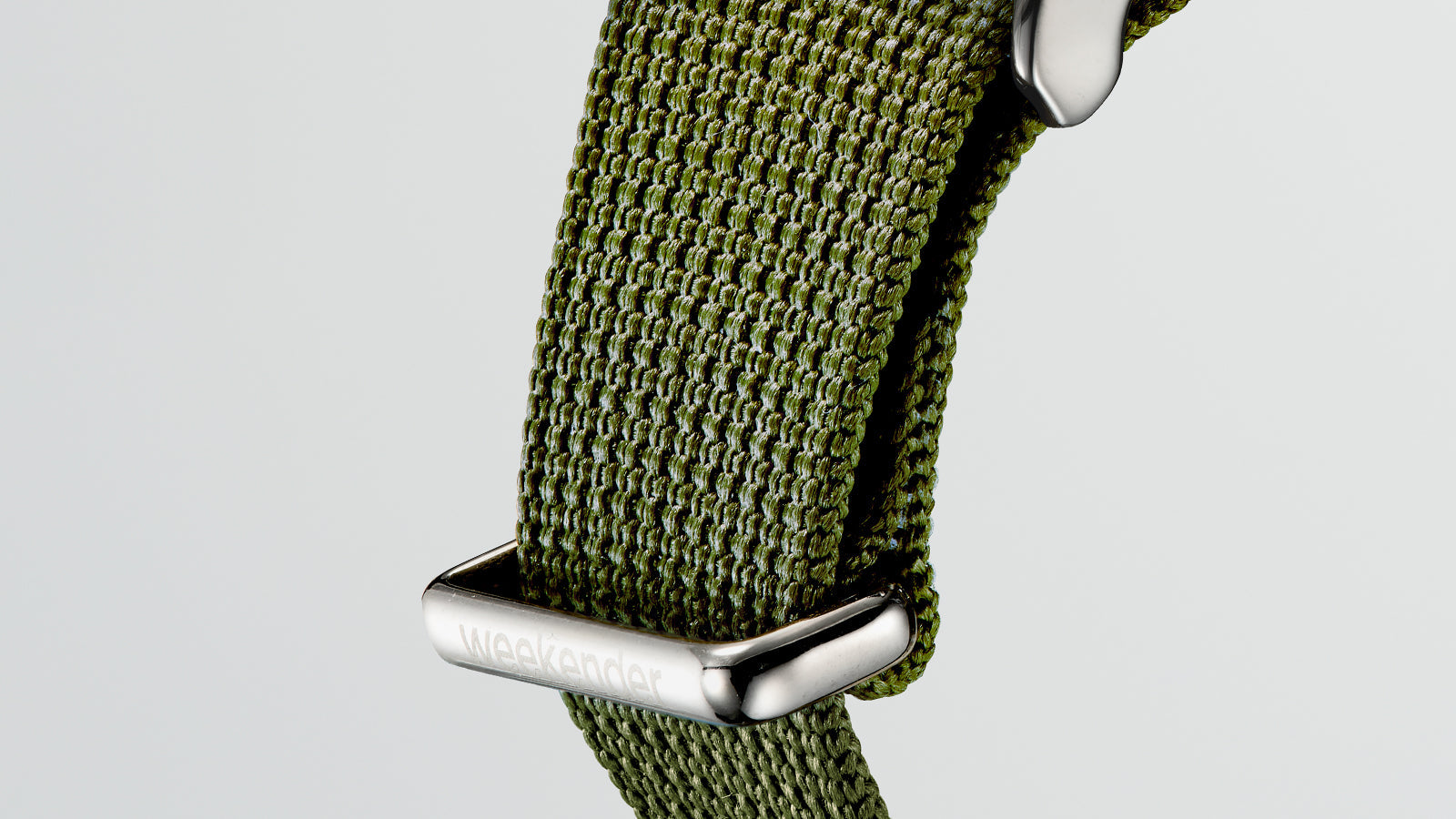 Close-up of the textured green fabric strap of the Timex Weekender with polished “weekender” engraving on the loop.