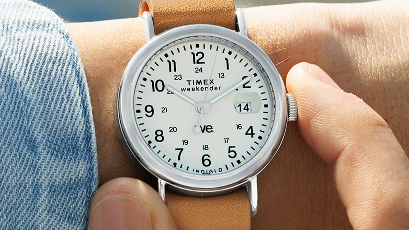 Person adjusting the crown of a Timex Weekender watch with white dial and tan leather strap, close-up wrist shot.