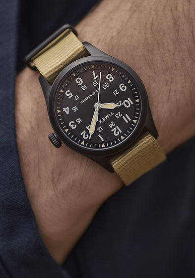The Timex Expedition Field Post Solar watch with black dial and khaki strap worn on the wrist, paired with a navy jacket for an outdoor-inspired look.