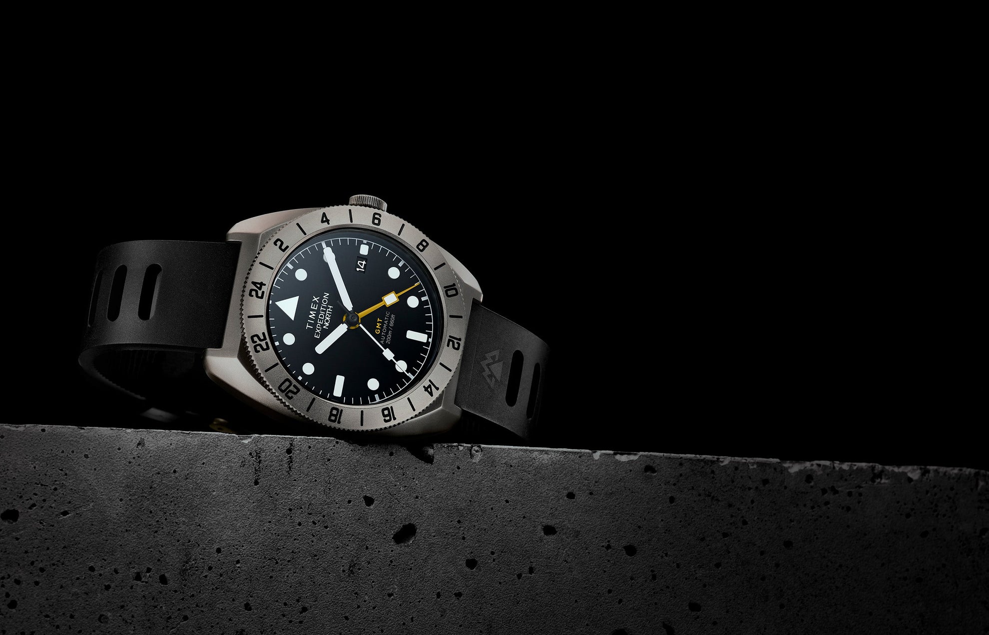 The Timex Expedition North GMT Titanium Automatic displayed against a black background, showcasing its titanium case, black dial, and yellow GMT hand.
