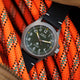 The Timex Expedition Titanium with a green dial and black strap positioned on bright orange climbing rope, emphasizing its rugged outdoor appeal.