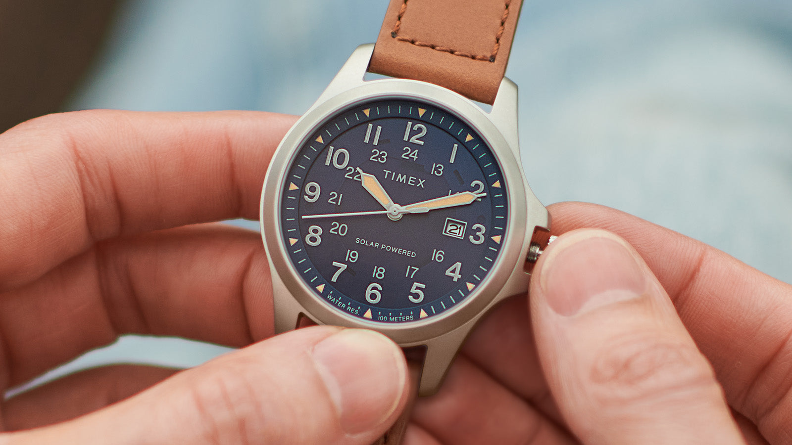 Timex Expedition Field Post Solar watch with a navy dial and silver-tone case shown in hand, with the crown being adjusted.