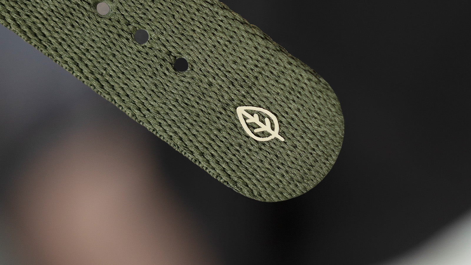Close-up of the green fabric strap of the Timex Expedition North Titanium Automatic watch, showing an embossed white leaf logo that highlights its eco-conscious design.