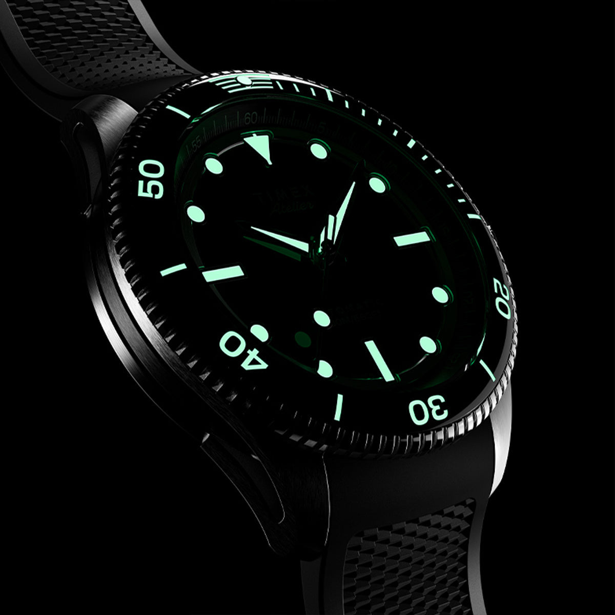 Detailed close-up of Timex Atelier automatic watch highlighting the knurled bezel edge, polished steel case, and crown engraved with the Timex “T” logo.