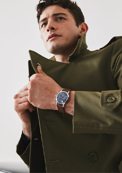 Man wearing Timex Marlin Chronograph Tachymeter with blue dial and brown leather strap while adjusting green coat collar.