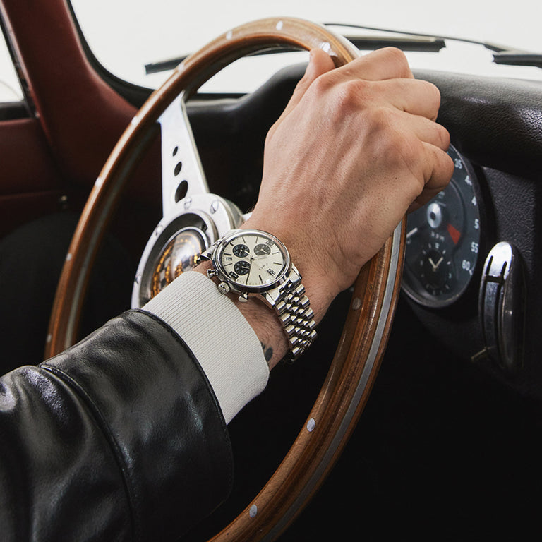 Close-up of man driving a vintage car wearing the Timex Marlin Chronograph Tachymeter with silver dial and stainless-steel bracelet.