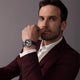 Model wearing Timex Marlin Chronograph Tachymeter with blue dial and brown leather strap, dressed in a burgundy suit.