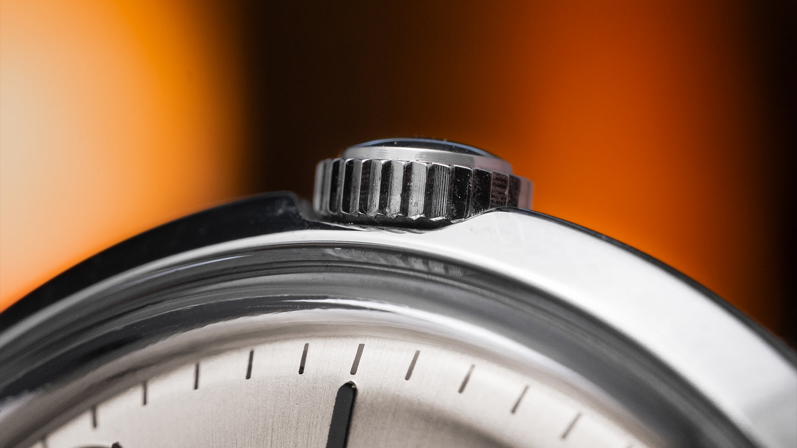 Close-up of the crown and polished stainless steel case of the Timex Marlin Hand-Wound watch, with brushed dial details in soft orange lighting.