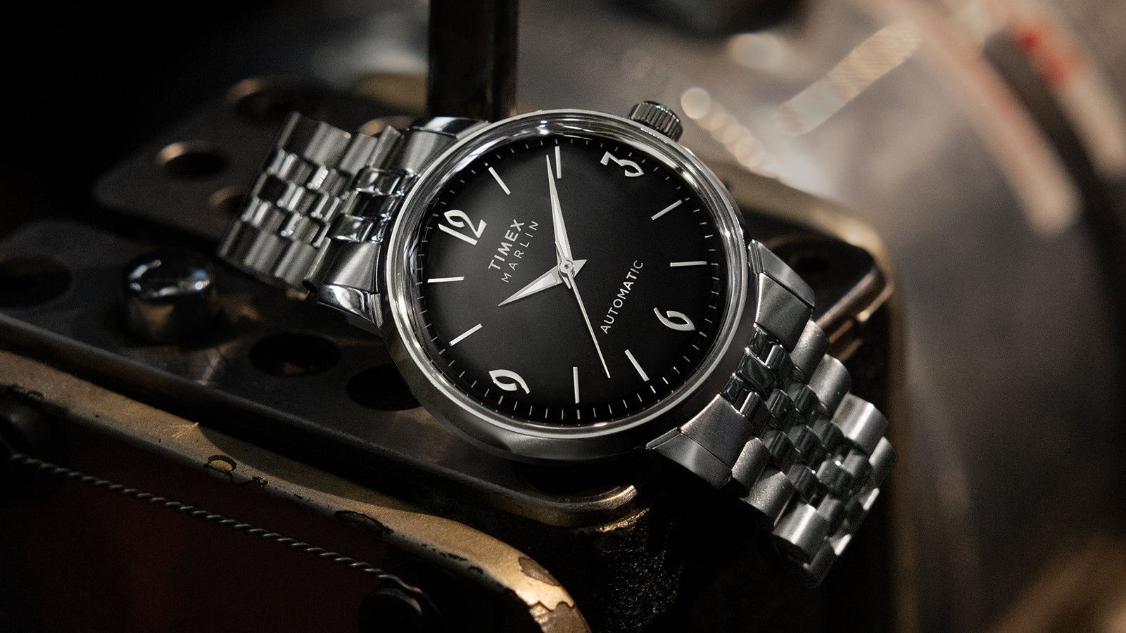 Timex Marlin Automatic with black dial and silver stainless-steel bracelet resting on a vintage metal surface.