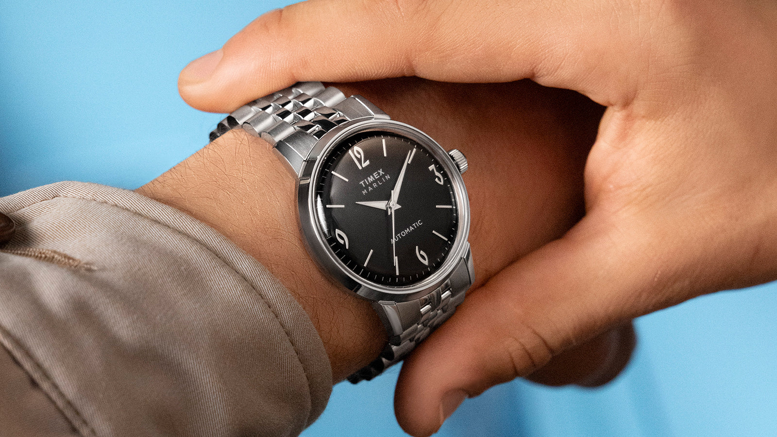 Timex Marlin Automatic with black dial and silver bracelet worn on wrist, paired with a light beige jacket.