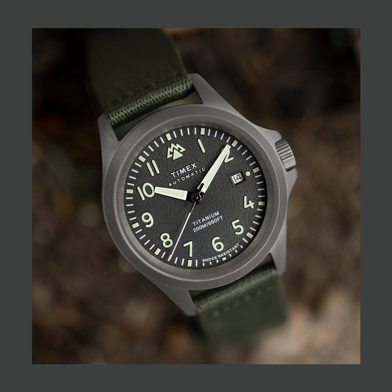 Timex Expedition North Titanium Automatic watch with a black dial, luminous numerals, and green fabric strap, photographed outdoors.