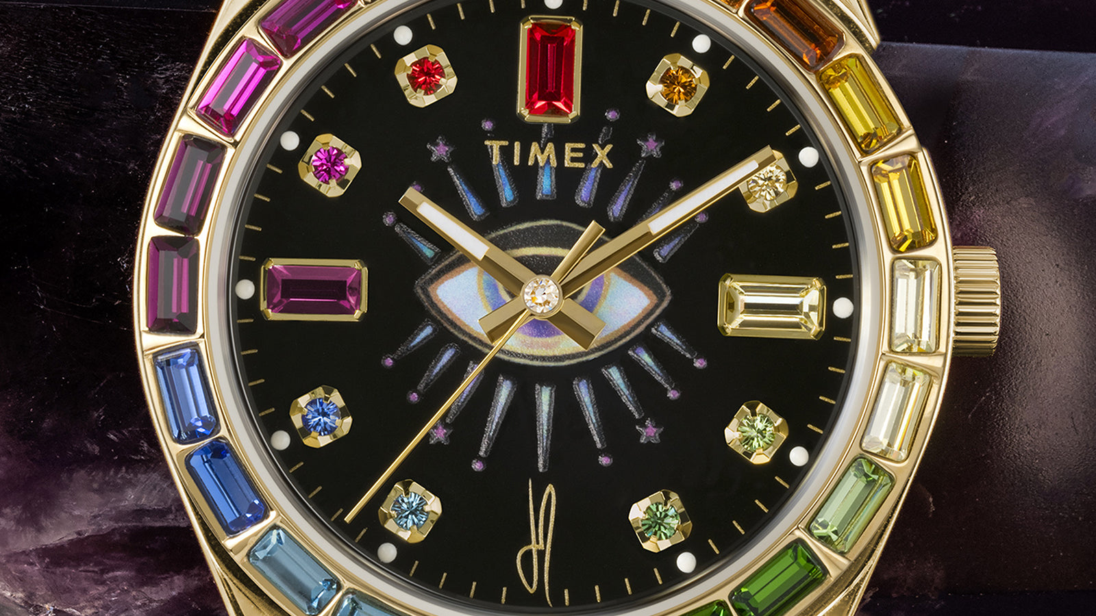 Macro image of the Timex x Jacquie Aiche “Cosmic Nights” dial, showcasing its gemstone hour markers and iridescent cosmic eye motif surrounded by gold-tone details.