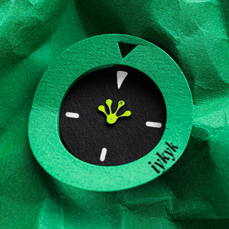 Close-up artistic shot of the Timex x seconde/seconde/ frog foot-shaped hour hand displayed within a green paper cutout resembling a watch face. Minimalist and creative, the image highlights the collaboration’s quirky design language.