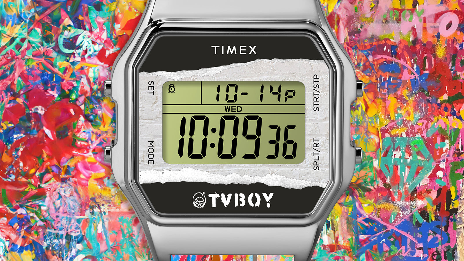 Close-up of the Timex T80 x TVBOY digital display showing time and date with the TVBOY logo on the lower bezel. The background bursts with abstract street-art graffiti in bold reds, blues, yellows, and greens.