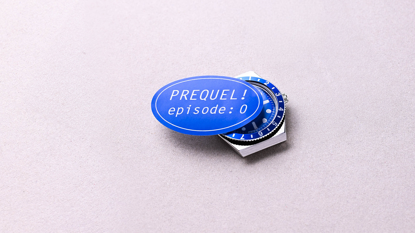 The blue Q Timex watch partially covered by a blue oval sticker reading “PREQUEL! episode: 0” on a neutral surface.