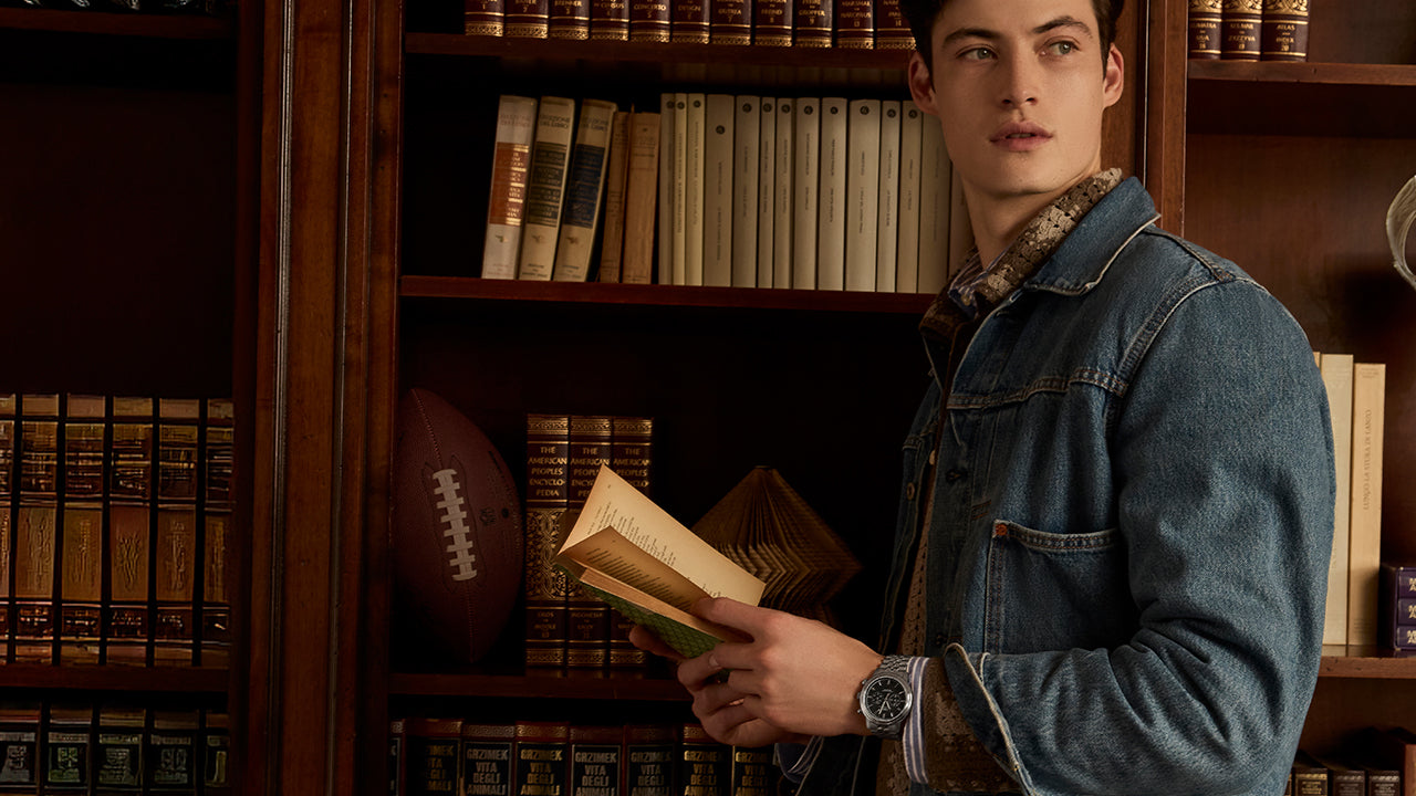 Man wearing the Timex Waterbury Metropolitan Chronograph while reading in a library, styled in denim jacket and casual layers.