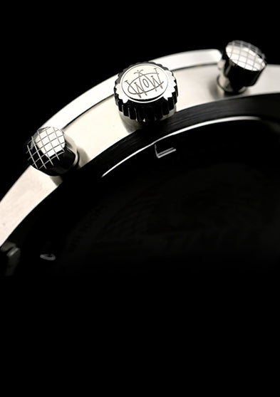 Detailed close-up of the Timex Waterbury Chronograph crown and pushers engraved with the Waterbury logo, showing brushed stainless steel finish.
