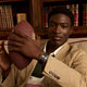 Man wearing the Timex Waterbury Heritage Chronograph with black and gold dial and brown leather strap while holding a football in a library setting.