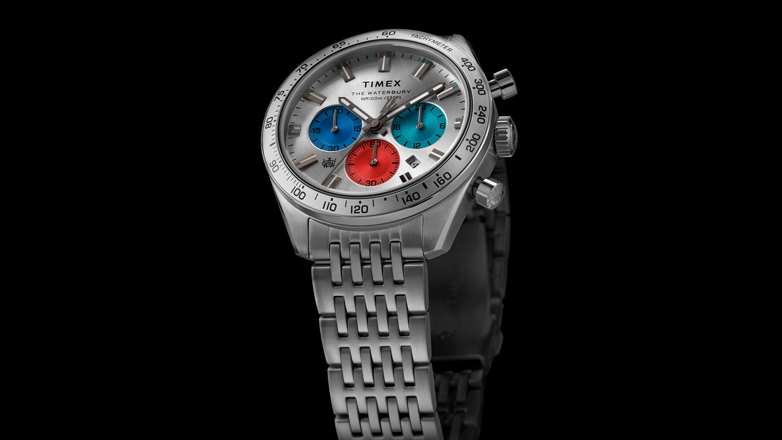 Timex Waterbury Chronograph with silver case, tachymeter bezel, and tricolor chronograph sub-dials against a black background.