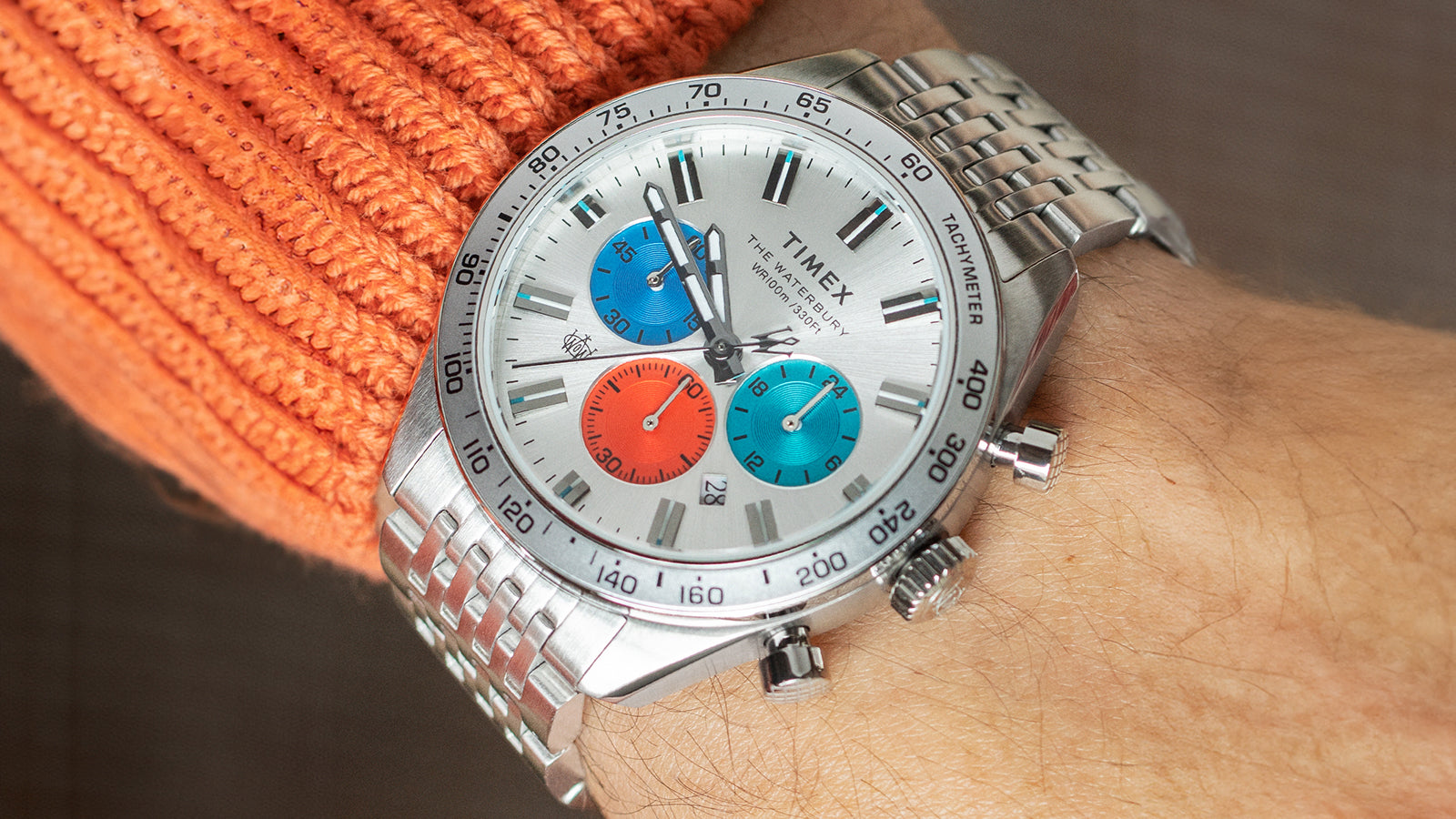 Timex Waterbury Chronograph on wrist with silver-tone stainless steel bracelet, featuring a silver dial and vibrant red and blue sub-dials under natural light.