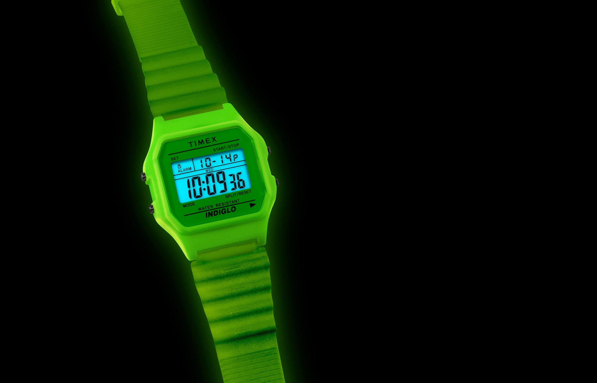 TIMEX® T80 digital watch illuminated with bright green INDIGLO® backlight in a dark setting, showing the display clearly glowing blue.