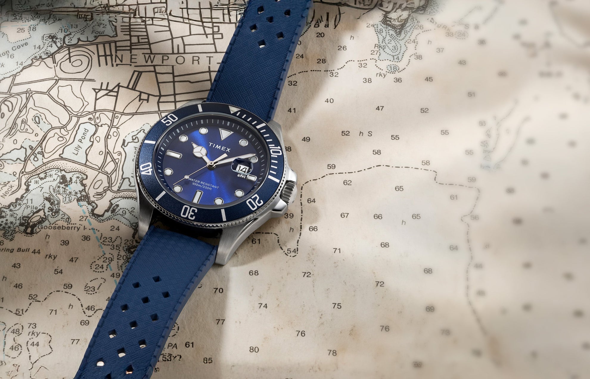 Timex Harborside Coast watch with a blue dial and bezel, featuring a textured blue strap, placed on a nautical map of Newport.
