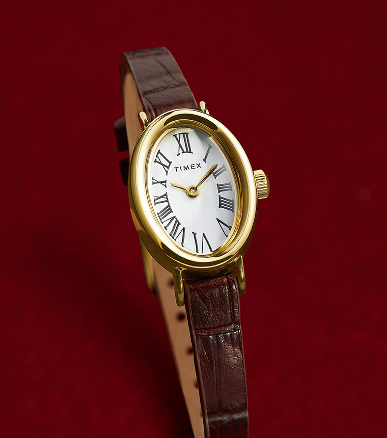 TIMEX® Cavatina watch with gold-tone case and brown leather strap displayed on a rich red background, highlighting its elegant silhouette.