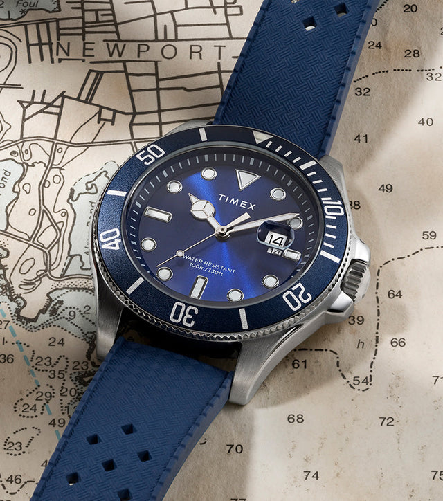 Timex Harborside Coast watch with a blue dial and bezel, featuring a textured blue strap, placed on a nautical map of Newport.