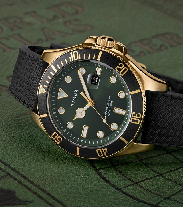 Timex Harborside Coast watch with a green dial, black bezel, and gold-tone stainless-steel case on a textured black strap, displayed on a vintage green world map background.