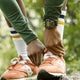 Runner wearing the TIMEX® IRONMAN® Flix 100 watch, tying orange sneakers in a green outdoor setting before a workout.