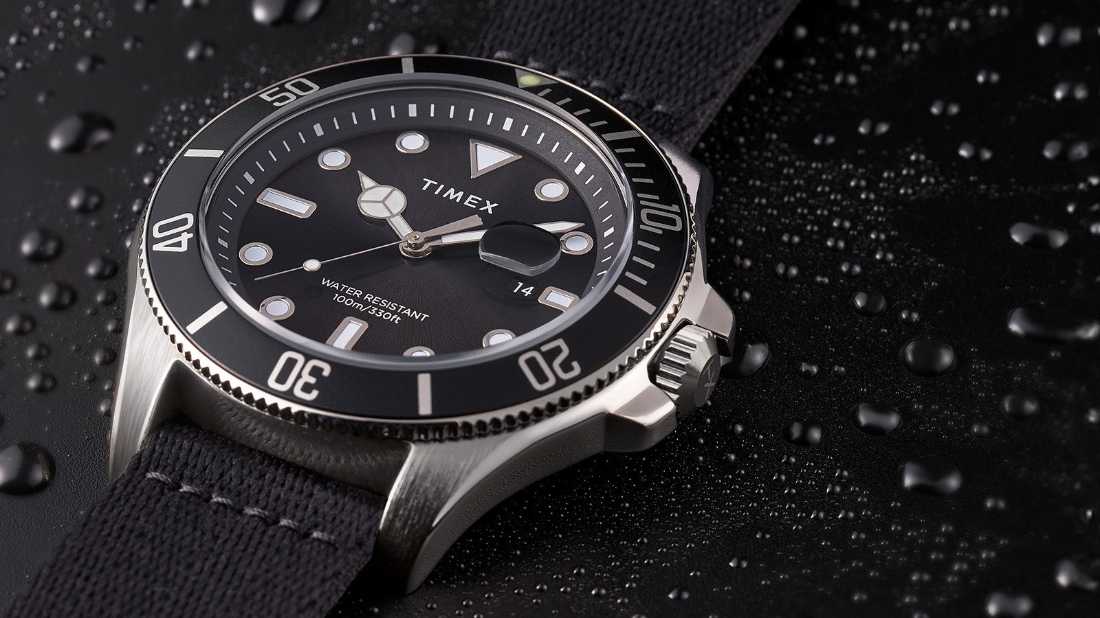 TIMEX® Harborside Coast watch with black dial and black fabric strap resting on a water-dappled black surface, showcasing its water-resistant design.
