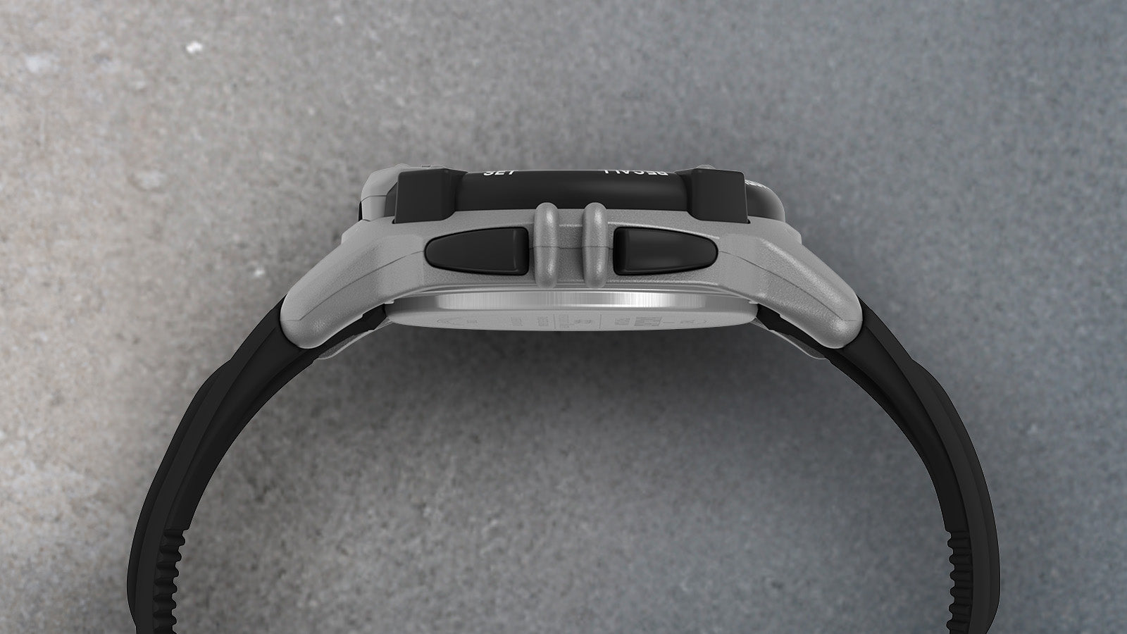 Side profile of the TIMEX® IRONMAN® Flix 100 digital watch showing its gray case, black buttons, and strap curvature on a textured surface.