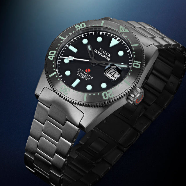 Timex Deepwater Reef 200 Titanium watch displayed at an angle, highlighting the black dial, aqua luminescent markers, titanium bezel, and matching titanium bracelet.