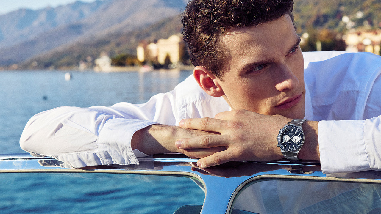 Model wearing the Q Timex Continental Chronograph with blue dial and stainless steel bracelet while leaning on a boat by the water.