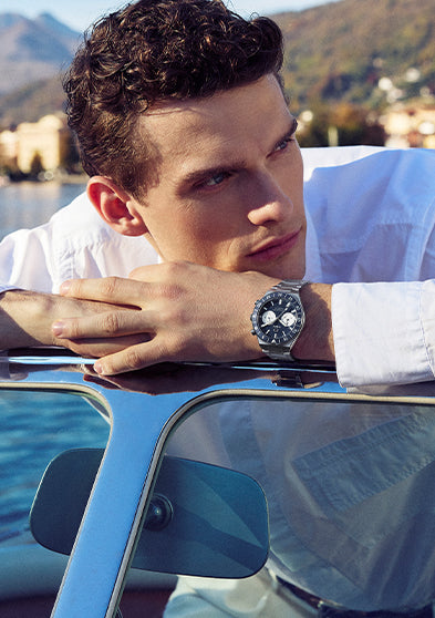 Model wearing the Q Timex Continental Chronograph with blue dial and stainless steel bracelet while leaning on a boat by the water.