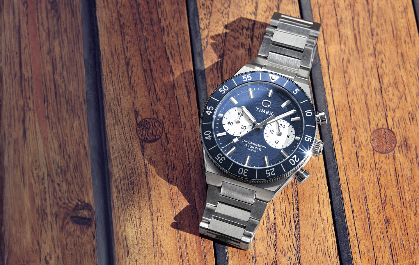 Timex Q Continental Chrono stainless steel watch with a blue dial, white chronograph subdials, and rotating blue bezel, photographed on a wooden surface.
