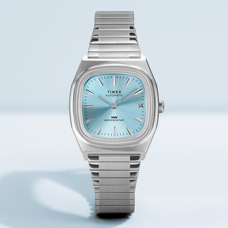 Front view of the Timex® Automatic 1983 E Line watch featuring a light blue dial, silver-tone case, and stainless steel expansion bracelet on a clean background.