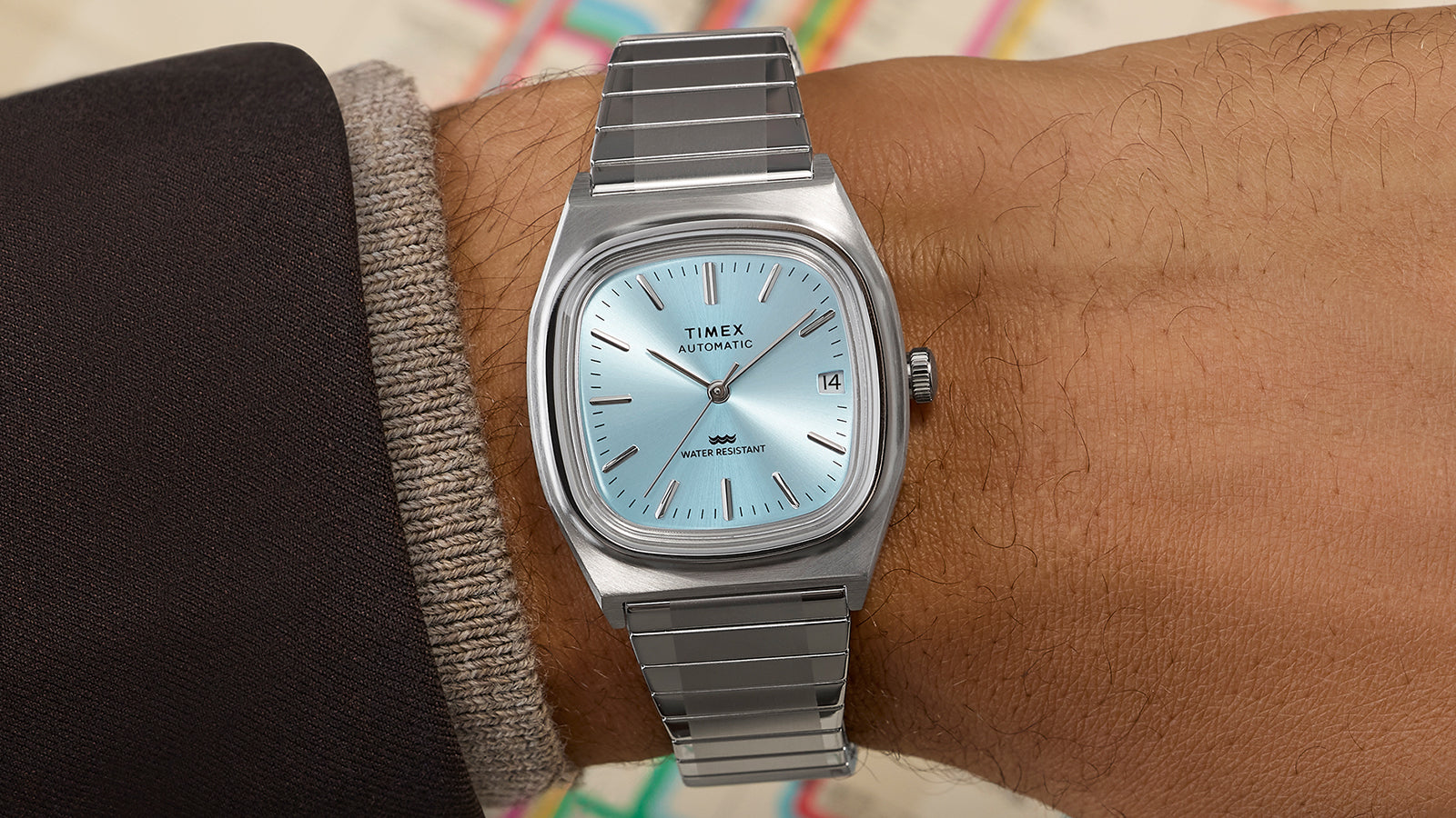 Timex® Automatic 1983 E Line stainless steel watch with light blue dial worn on wrist, highlighting the square case and expansion bracelet.